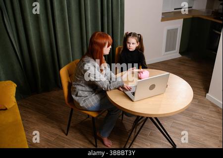 La fille est assise à table avec un tuteur privé et elle parle à l'élève de la littératie financière, de l'épargne, montrant des diapositives éducatives sur ordinateur portable. Concept enseignement privé, enseignant Banque D'Images