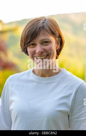 Femme de 50-55 ans souriante profitant d'une chaude journée ensoleillée à l'extérieur Banque D'Images