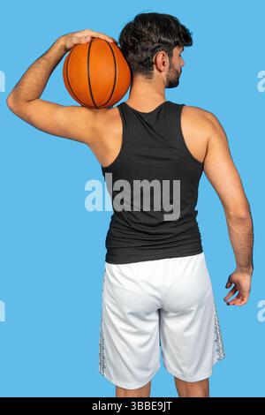 Joueur de basket-ball tenant la balle sur l'épaule, vue arrière, isolé sur fond bleu Banque D'Images