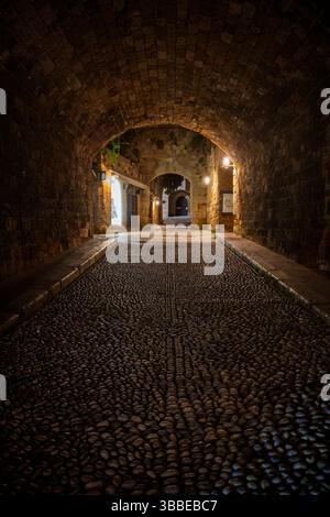 Rue pavée idyllique et vide et tunnel au site médiéval du patrimoine mondial de l'UNESCO de la vieille ville de Rhodes sur l'île de Rhodes en Grèce la nuit. Banque D'Images