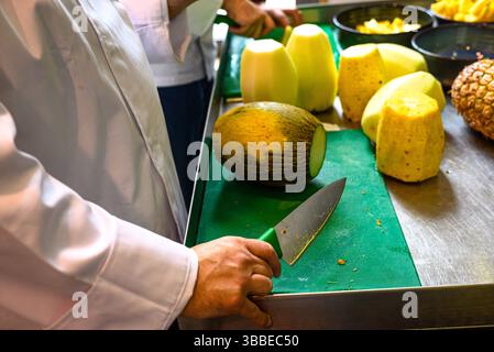 mains d'un cuisinier hachant des melons frais et des ananas dans une cuisine Banque D'Images