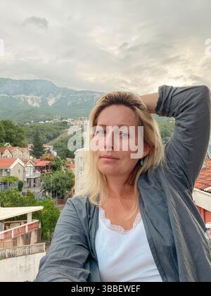 Femme d'âge moyen jouissant d'une vue imprenable sur la montagne sur le balcon tôt le matin d'été Banque D'Images
