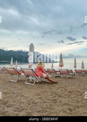 Femme assise sur un transat sur une plage vide tôt le matin et profitant de la belle vue Banque D'Images