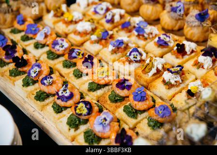 Petits canapés élégants garnis de crevettes, pesto, mélange bruschetta et fleurs comestibles, servis sur du pain grillé pour les événements de restauration. Banque D'Images
