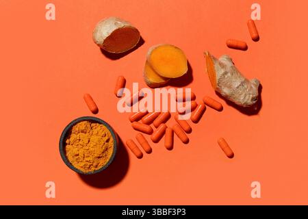 Composition avec de la poudre de curcuma et des pilules sur fond orange, vue de dessus Banque D'Images
