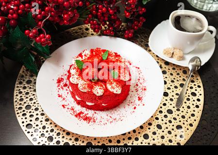 Gâteau de velours rouge vif garni de fraises et de crème, servi avec un café noir chaud et des cubes de sucre sur le côté. Banque D'Images
