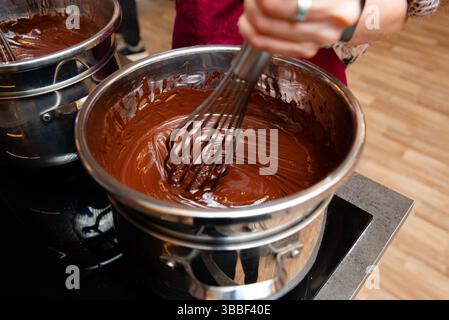 Gros plan de chocolat fondu épais battu dans une chaudière double sur une cuisinière pendant la préparation du dessert ou la cuisson. Banque D'Images