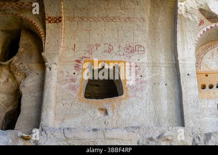 Des motifs géométriques d'ocre rouge et une fenêtre sculptée décorent un mur plat dans l'église sombre, Goreme, montrant une ornementation byzantine simple. Banque D'Images