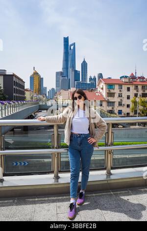 Brunette en lunettes de soleil sourit à la caméra sur le viaduc de Shanghai avec les gratte-ciel de Pudong avec Shanghai Tower, World Financial Center et Jin Mao Tower BEH Banque D'Images