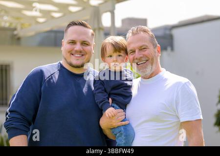 Trois générations d’une même famille se rassemblent dans un jardin ensoleillé – grand-père, père et enfant. Banque D'Images