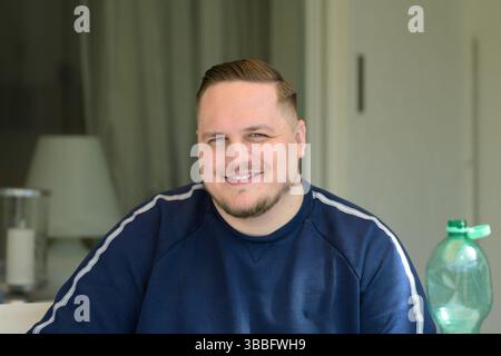 Un jeune homme dans un sweat-shirt bleu marine sourit chaleureusement à la caméra dans un cadre intérieur légèrement éclairé. Banque D'Images