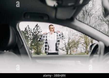 Jeune homme ajustant la veste près de la voiture à l'extérieur Banque D'Images