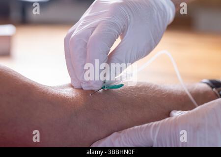 Mains gantées insérant l’aiguille IV dans le bras du patient Banque D'Images
