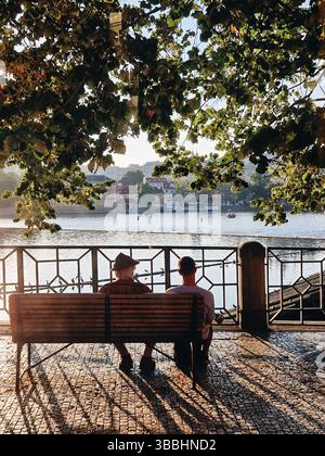 Couple assis sur un banc au bord de la rivière pendant une heure dorée Banque D'Images