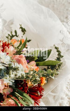 Gros plan coloré et ensoleillé d'un bouquet de mariée sur une robe en dentelle blanche Banque D'Images