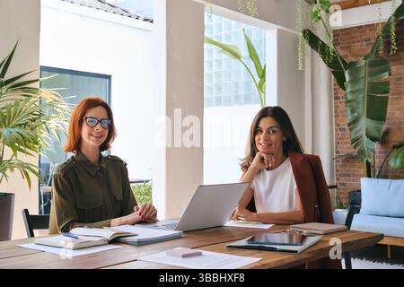Portrait de deux femmes d'affaires heureuses assis au bureau de travail avec ordinateur portable. Banque D'Images