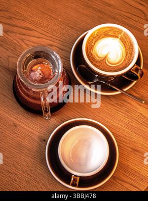 Vue de dessus d'un cappuccino avec mousse en forme de coeur, théière en verre et soucoupe sur une table en bois. Banque D'Images