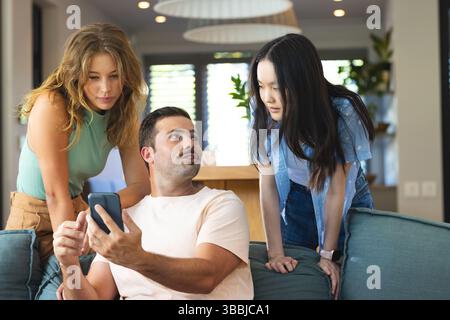 Divers amis se réunissant autour du smartphone dans le salon sur le canapé bleu-gris, avec table basse Banque D'Images