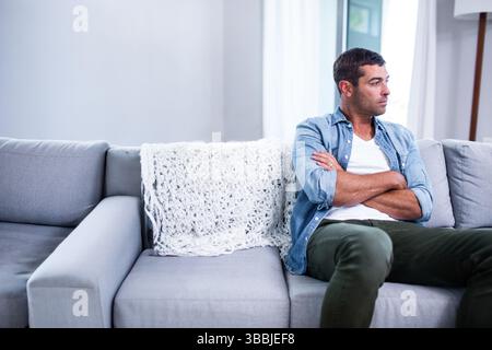 Homme assis regardant dehors sur un canapé gris dans le salon, avec couverture tricotée, espace copie Banque D'Images
