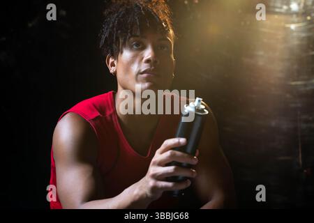 Tenant l'homme afro-américain dans le mur de pulvérisation de chemise rouge dans le studio, avec la peinture en aérosol noire peut Banque D'Images