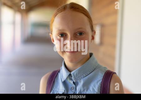 Élève fille souriante debout dans le couloir de l'école, avec des sangles de sac à dos violettes Banque D'Images