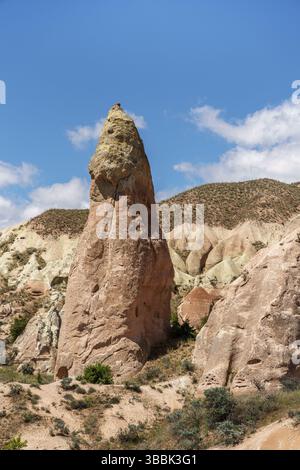 Un seul sommet rocheux haut s'élève au-dessus du fond de la vallée dans la Vallée Rouge de Cappadoce, entouré de buissons verts bas et d'espaces ouverts. Banque D'Images