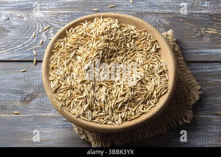 Gros plan de grains d'avoine crus dans un bol en bois placé sur un tissu en toile de jute, vu d'en haut. Composition de style rustique sur une table en bois pour la nourriture et Banque D'Images