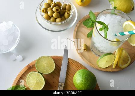 Comptoir de cuisine avec boisson rafraîchissante à base de menthe, citron et citron vert, avec planche à découper et fruits et récipients avec glace et olives. Vue de dessus. Banque D'Images