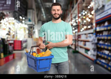 Homme tenant panier avec différents produits alimentaires au supermarché Banque D'Images