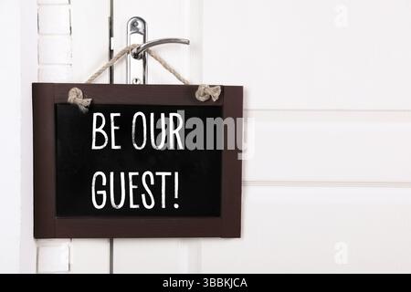 Petit tableau noir avec phrase Be our Guest accroché sur la poignée de porte, espace pour le texte Banque D'Images