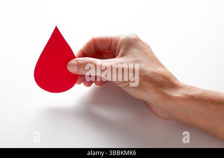 Une main féminine tenant une goutte symbolique de sang. Concept de don de sang. Banque D'Images