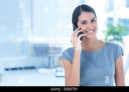 Femme parlante debout dans un espace de bureau, tenant un smartphone près du clavier et de l'usine, copiez l'espace Banque D'Images