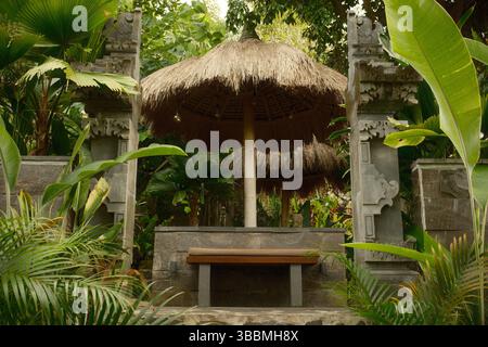 Un banc de repos de style balinais traditionnel avec toit de chaume et piliers de portail en pierre Banque D'Images
