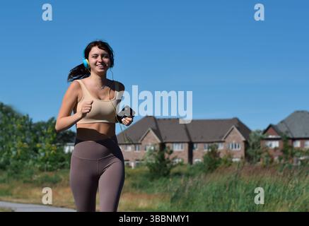 Jeune femme avec des écouteurs souriant jogging heureux à l'extérieur Banque D'Images