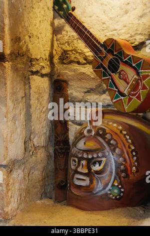 Une collection dynamique d'art populaire est disposée sur une étagère en pierre, avec une guitare peinte, des masques traditionnels et des figures en bois sculptées, mettant en valeur Cu Banque D'Images