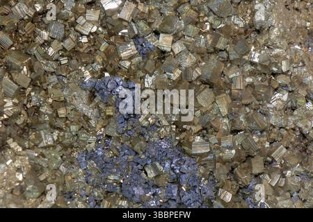 Une vue rapprochée de divers cristaux affichant des teintes d'or et de bleu profond, nichés parmi les roches grises sous la lumière naturelle, soulignant le complexe de Banque D'Images