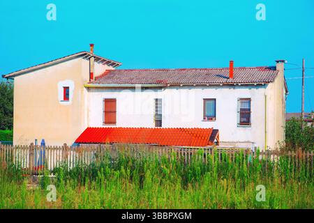 Scène rurale calme, avec une maison avec un toit de tuiles rouges, nichée derrière une simple clôture en bois et de l'herbe envahie Banque D'Images