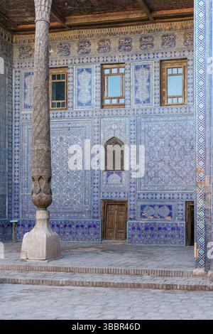 Un mur carrelé bleu et blanc avec des piliers en bois et des détails sculptés se dresse dans la cour du palais Tash Khauli à Khiva Ouzbékistan. Banque D'Images