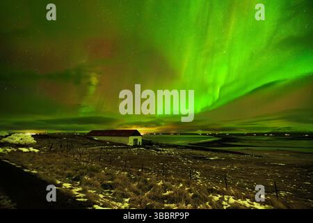 Belle lumière nordique dansant sur une grange au bord de la mer en Islande Banque D'Images