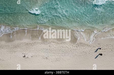 Drone vue aérienne des vagues lavant terre sur une plage de sable blanc avec deux touristes marchant, profitant de leurs vacances. Ayia Napa Chypre Banque D'Images