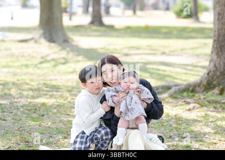 Au printemps, dans un parc de Fukuoka, une maman dans la trentaine est assise avec son fils de 3 ans et sa petite fille de 6 mois. Ils sourient pour la caméra. Cette photo sh Banque D'Images