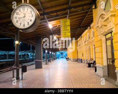 Gare éclairée avec des murs jaunes, une grande horloge, et plate-forme s'étendant sous un toit en bois la nuit, Plovdiv Banque D'Images