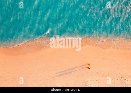 Vue aérienne panoramique plage tropicale vagues sable couple marchant de longues ombres soleil nature sereine magnifique vacances d'été paysage île papier peint Banque D'Images