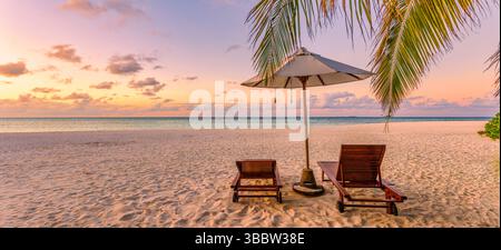Paysage de plage tropicale panoramique avec couple romantique assis sur des chaises, amour et détente par la scène de coucher de soleil de vacances d'été de la mer, rivage paisible Banque D'Images