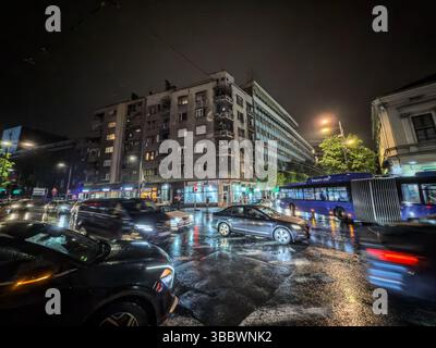 BELGRADE, SERBIE - 15 MARS 2025 : la circulation nocturne traverse le centre de Belgrade sous de fortes pluies. Phares, reflets d'asphalte mouillé, voitures floues Banque D'Images
