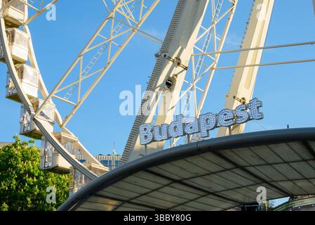 Le Budapest Eye se dresse haut contre un ciel bleu clair, mettant en valeur des couleurs vives et une atmosphère animée, invitant les visiteurs à profiter de la magnifique Banque D'Images