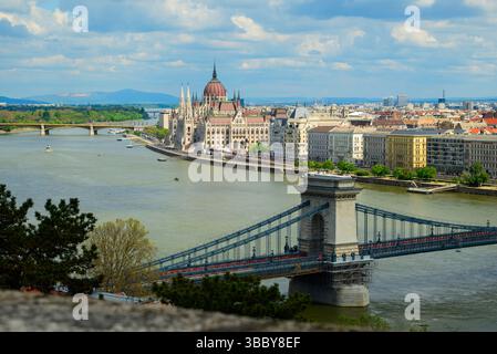 Une vue panoramique capture le bâtiment emblématique du Parlement de Budapest le long du Danube, avec le pont des chaînes qui enjambe élégamment l'eau sous un Banque D'Images