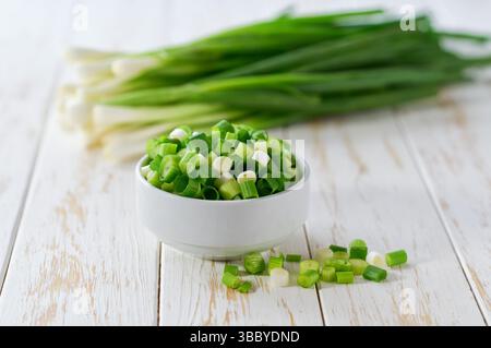 Des échalotes hachées ou de jeunes oignons de printemps dans un bol en céramique , sur une table de cuisine. Banque D'Images