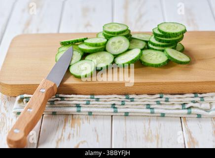 tranches de concombres biologiques hachées sur une planche à découper, sur une table de kithen blanc. Banque D'Images