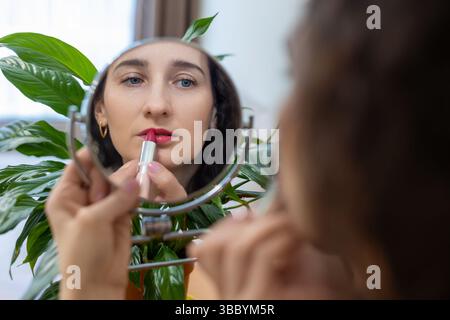 Femme appliquant du rouge à lèvres tout en regardant dans le miroir. Banque D'Images
